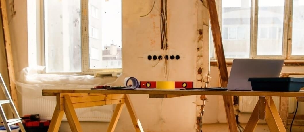 Apartment renovation with tools, blueprints, and laptop on a workbench.