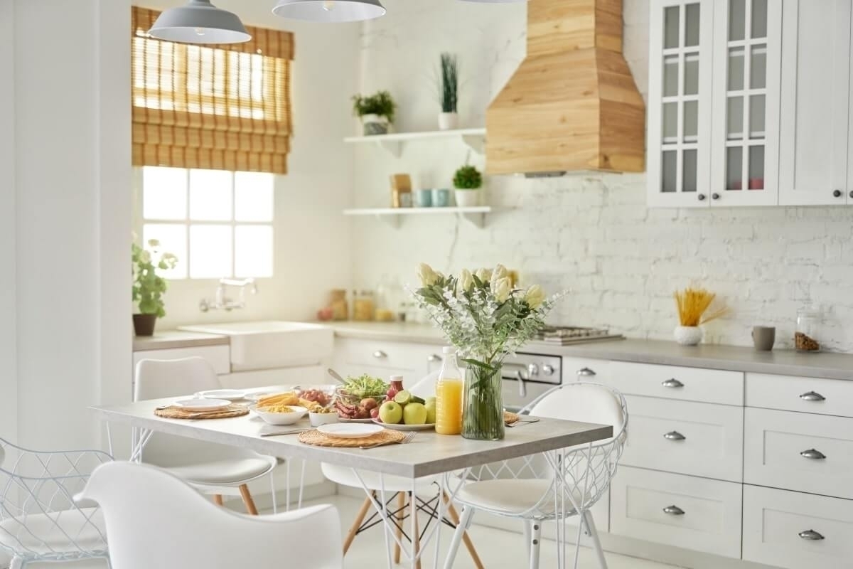 Bright white kitchen with table setting, flowers, and wooden accents.