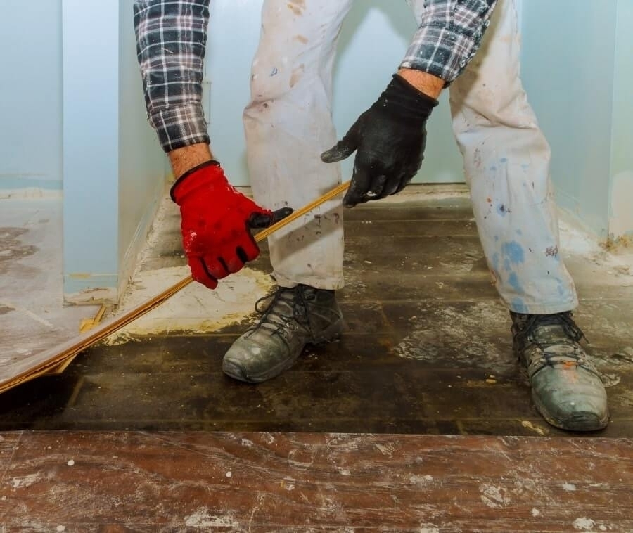 Worker removes old laminate flooring plank.