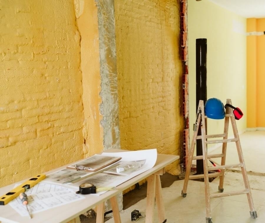 Yellow brick wall renovation with blueprints, tools, and safety gear.